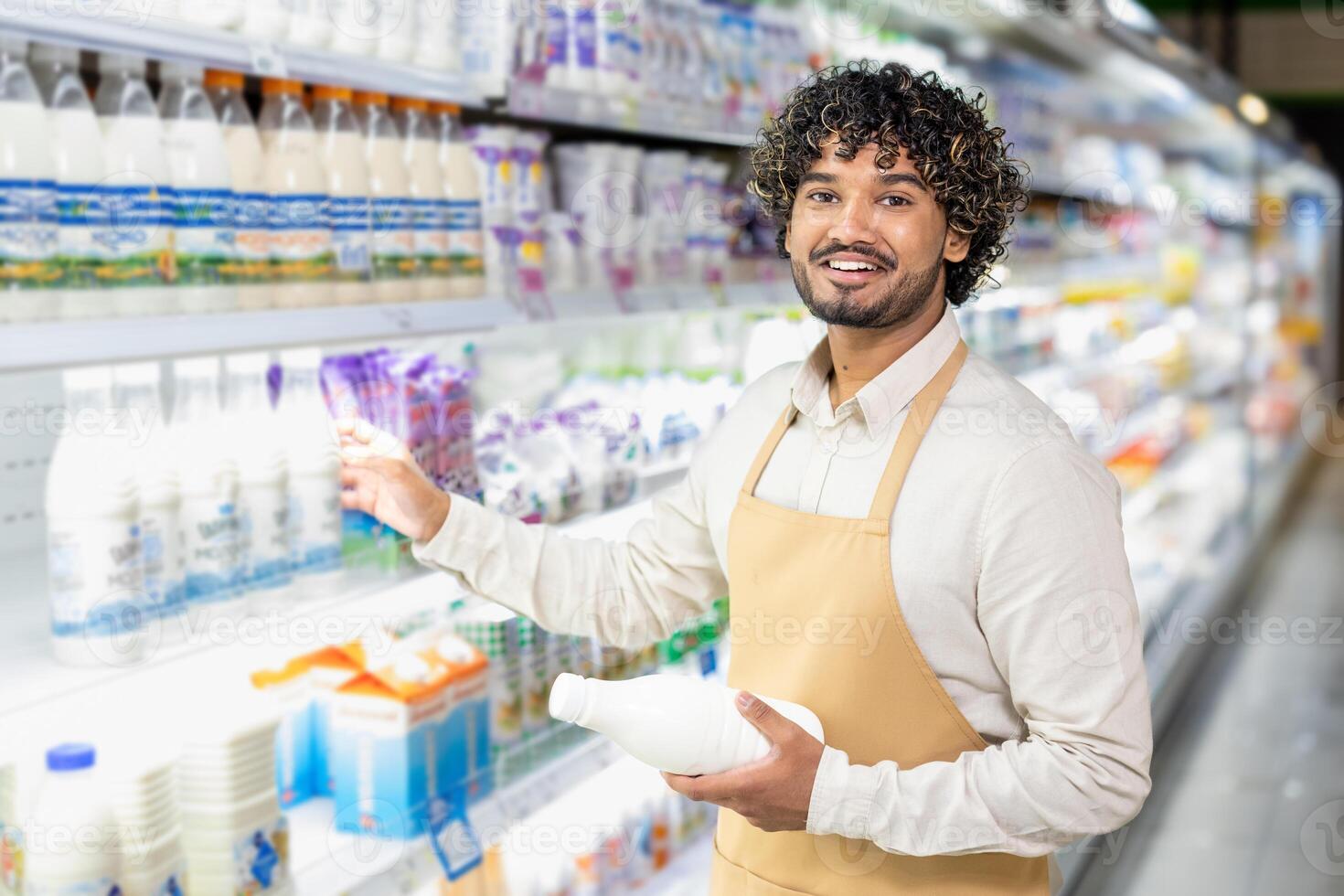 A smiling worker in a supermarket holds a milk bottle, restocking dairy products on the shelf. The focus is on customer service. photo