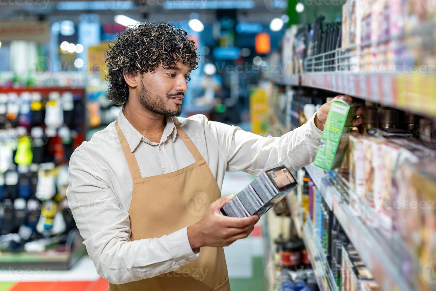 A friendly worker, wearing an apron, is reviewing products on the shelf at the store. He carefully considers the labels. photo