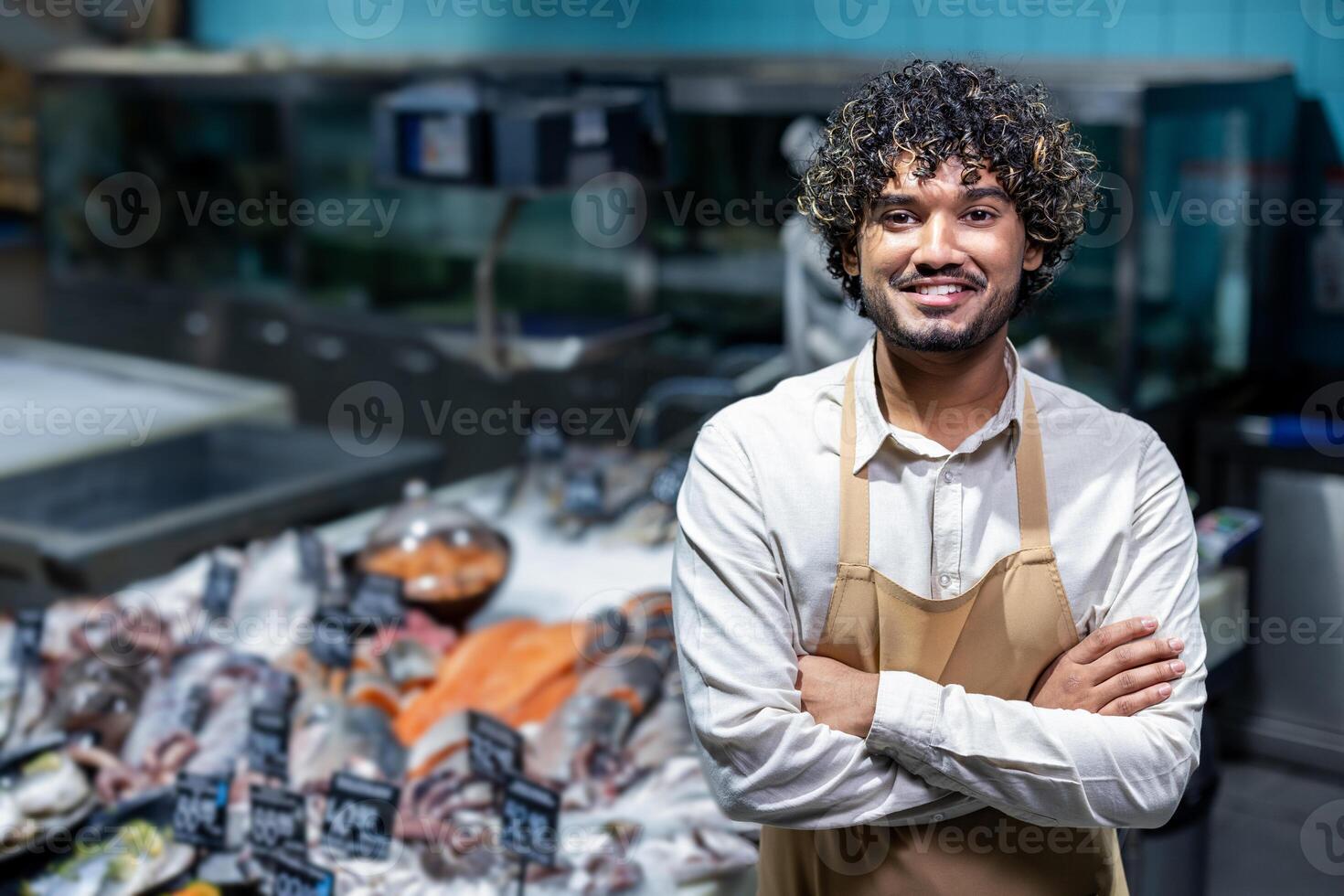 A smiling fishmonger stands confidently in front of a display of fresh seafood, ready to assist customers. He wears an apron. photo