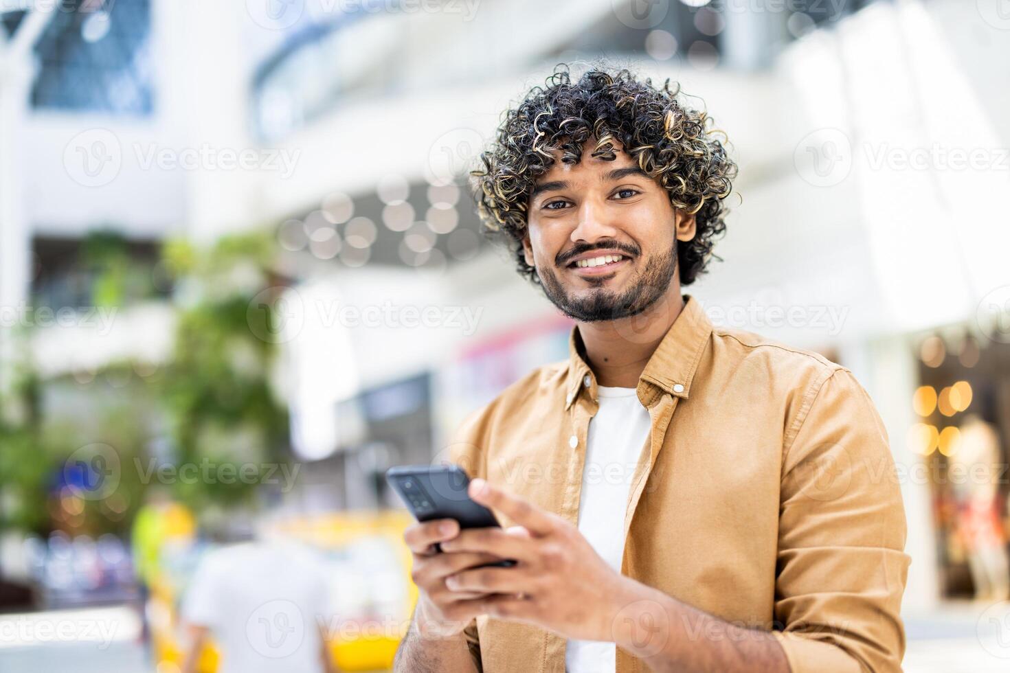 A smiling young man, holding his smartphone, is captured in a modern indoor environment, looking happy. photo