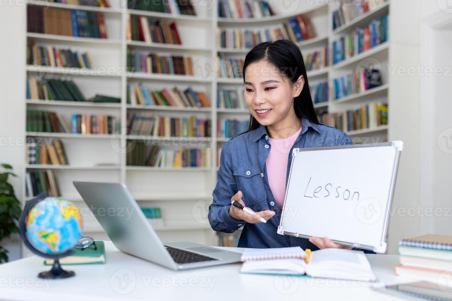 An asian woman gives an online lesson while holding a whiteboard with the word lesson in front of a laptop. photo