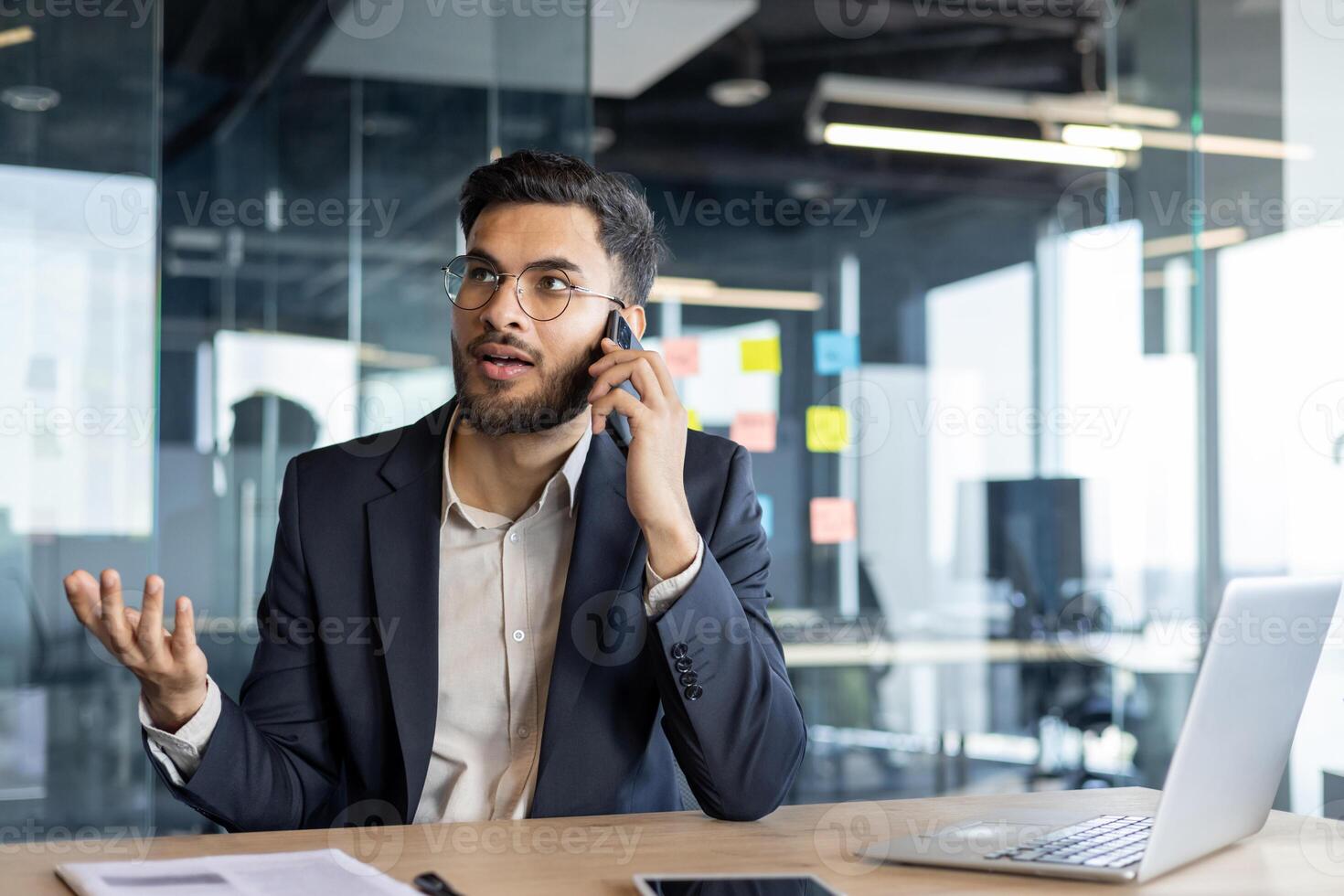 Serious confident businessman talking on the phone while sitting at the desk in the office. Successful man in a business suit, working. photo