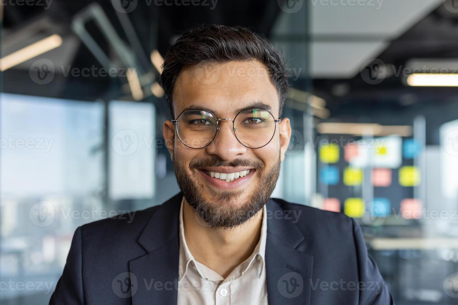Portrait of successful young businessman at workplace inside office. Man smiling close up and looking at camera, satisfied financier investor. photo