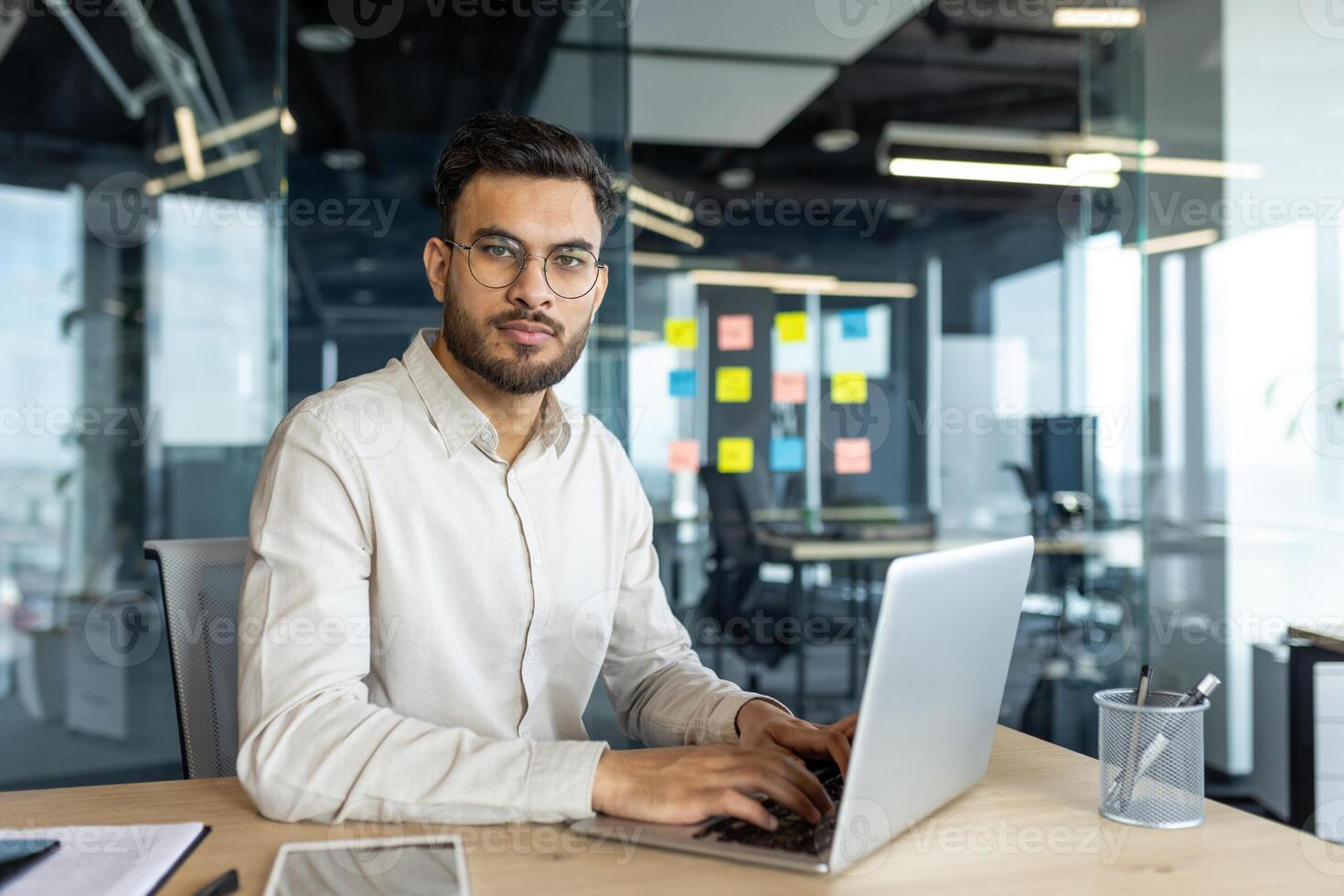 Portrait of mature and serious businessman at workplace. Man in shirt looking at camera, working with laptop inside office. photo
