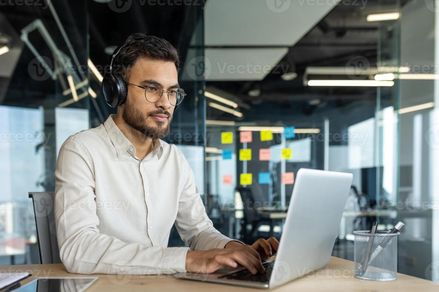 Serious thinking programmer coding new software. Man in headphones working with laptop inside office. Developer typing on keyboard. photo