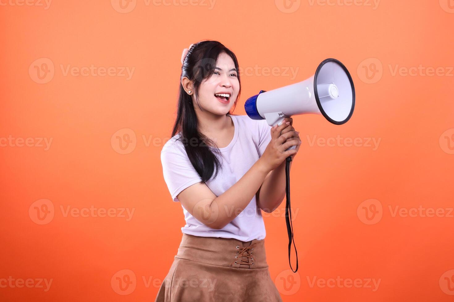 Young woman with dark hair holding a white megaphone and smiling against an orange background photo