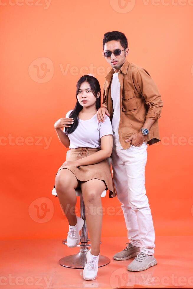 A man and a woman posing in a studio with an orange background wearing casual clothes photo