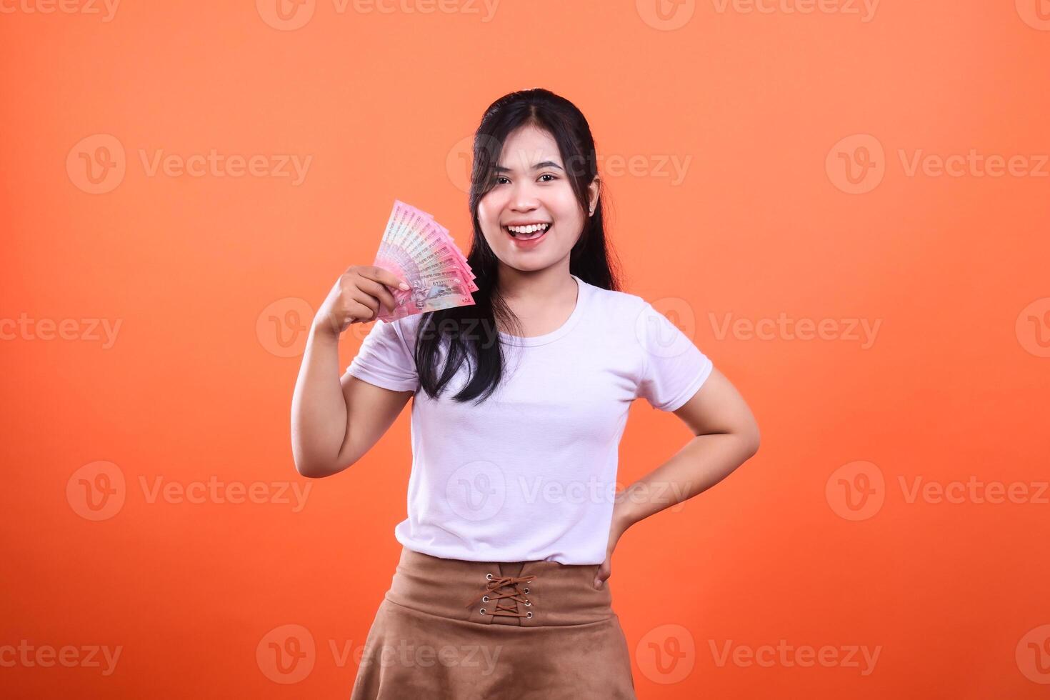 Smiling woman holding a fanned stack of Indonesian Rupiah on orange background photo