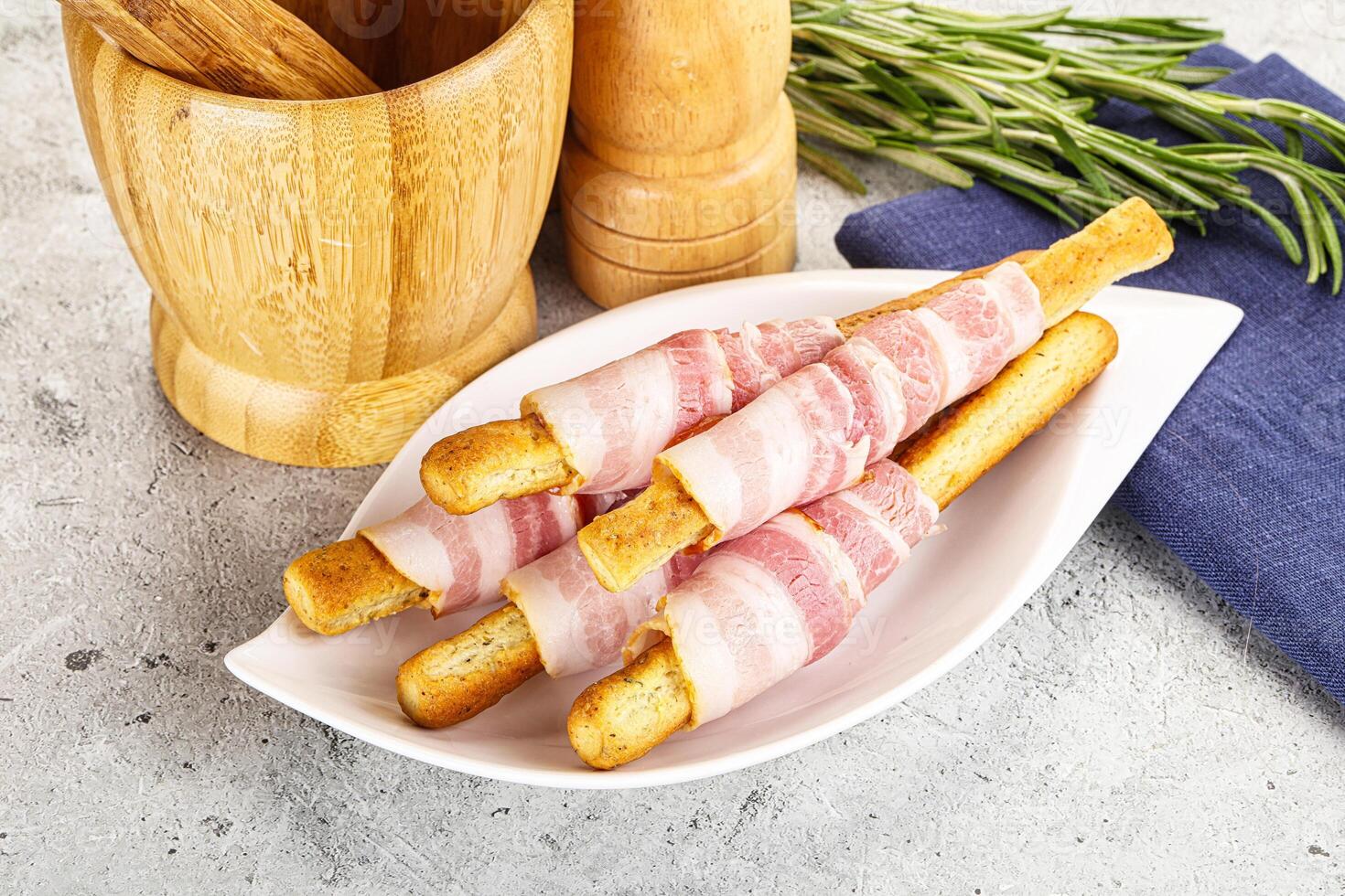 A plate with bacon wrapped bread sticks and a wooden spoon photo