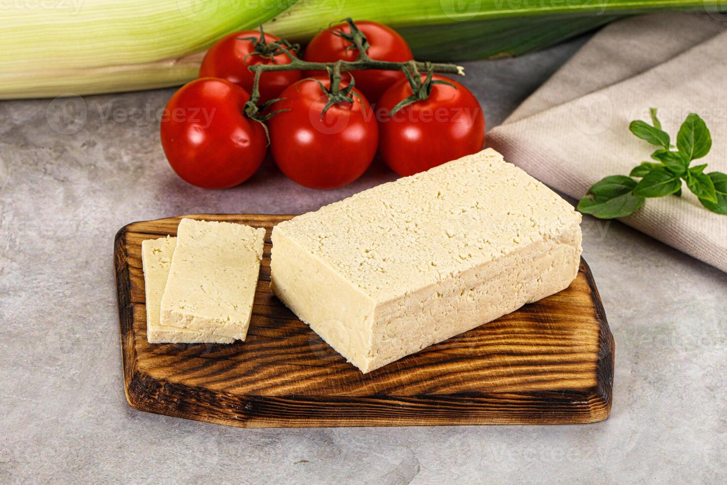 A piece of tofu on a cutting board next to tomatoes and corn photo