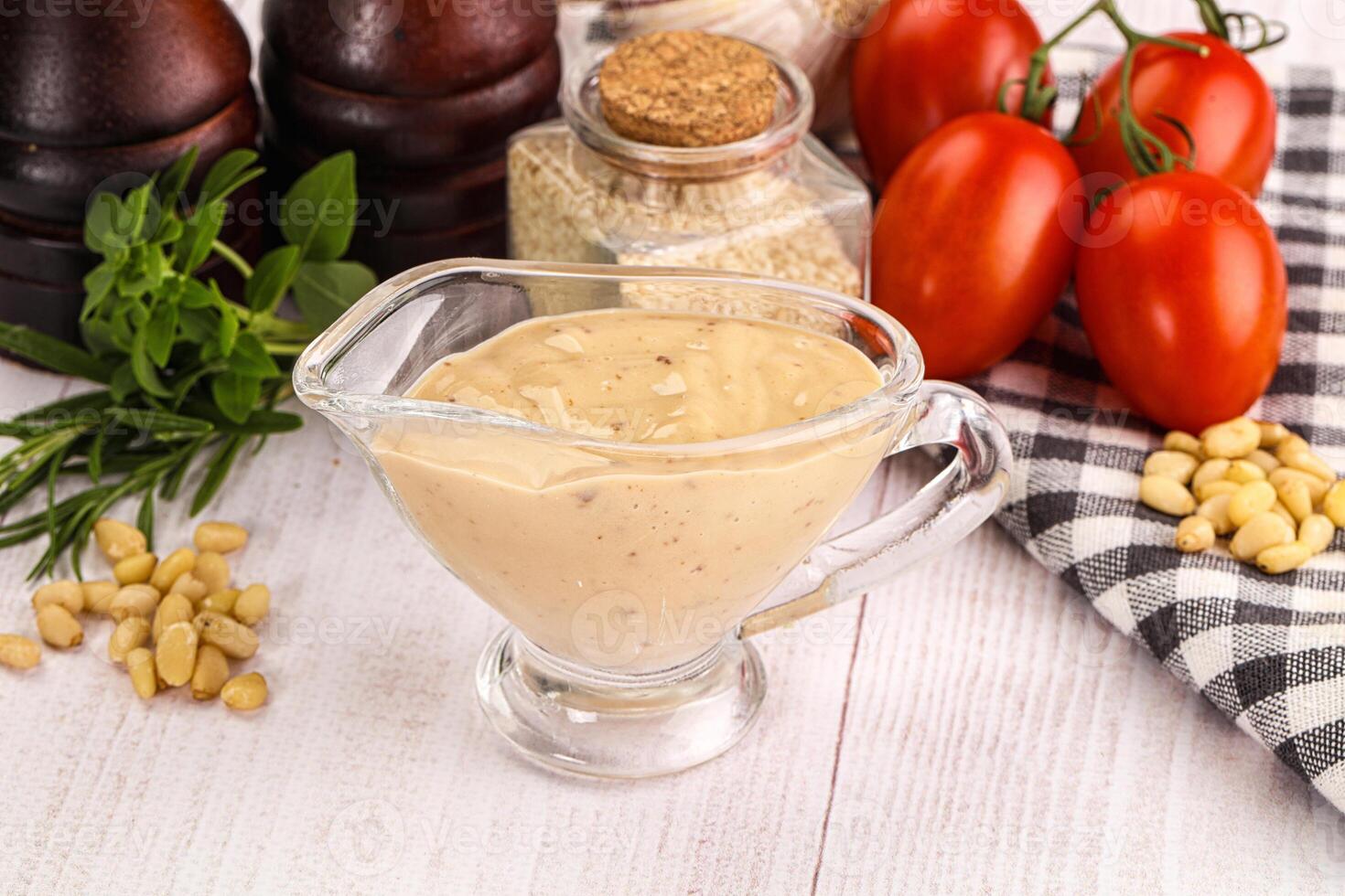 A glass of dressing sits on a table next to tomatoes, garlic and other ingredients photo