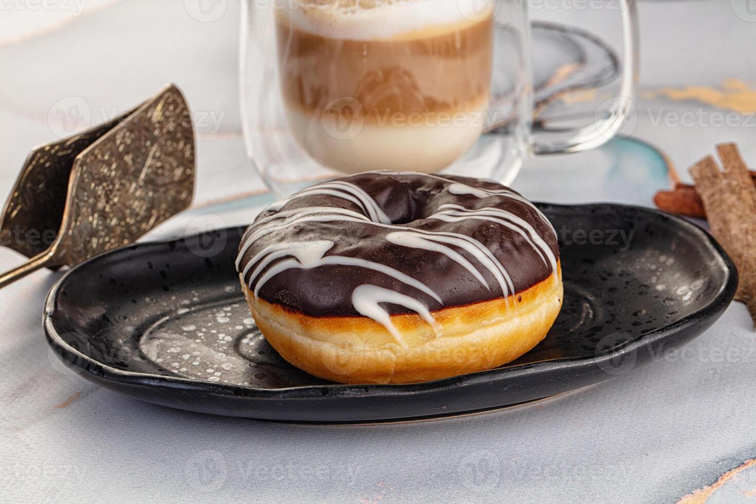 A donut on a plate with a cup of coffee and a spoon photo