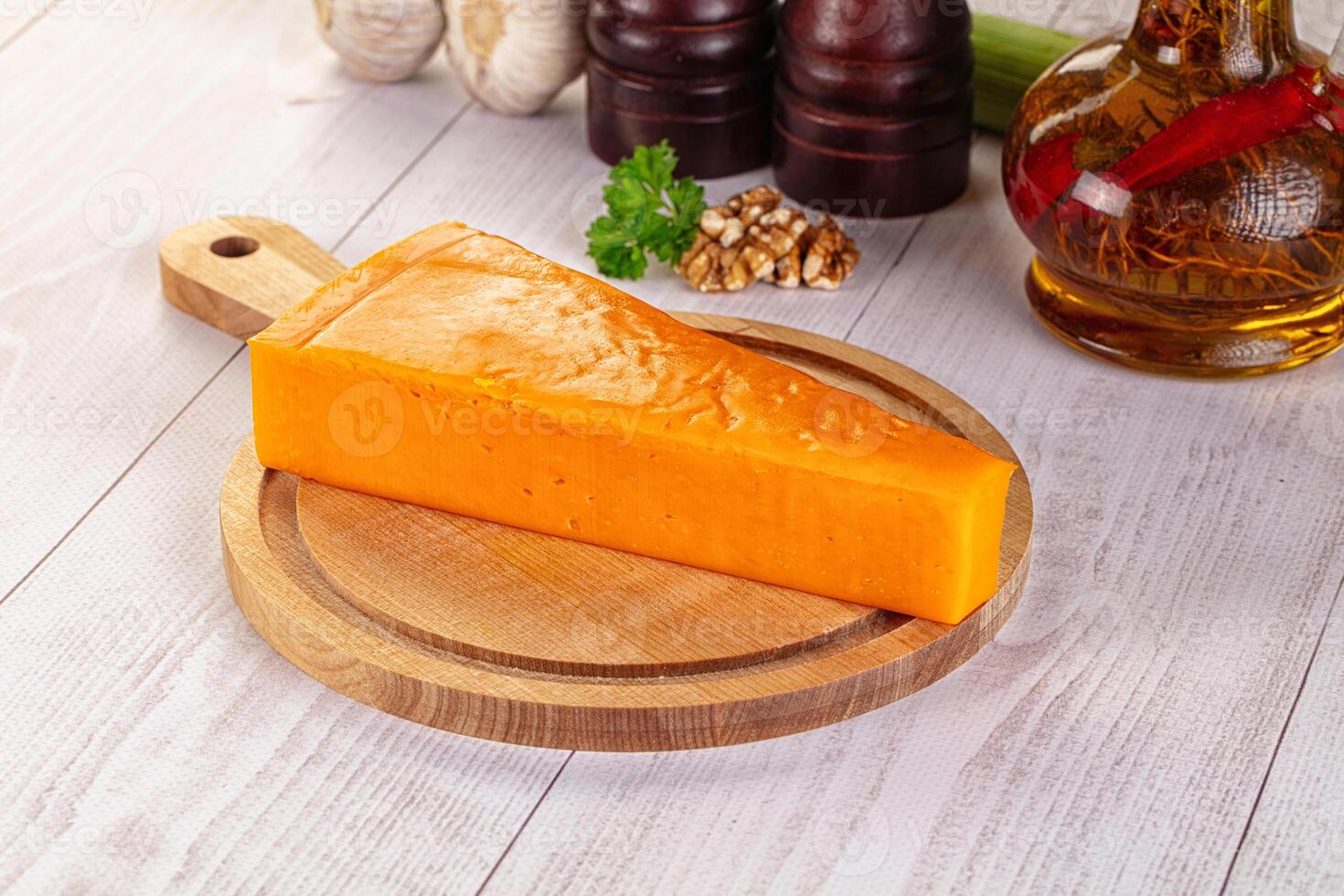 A piece of cheese on a wooden board next to other ingredients photo