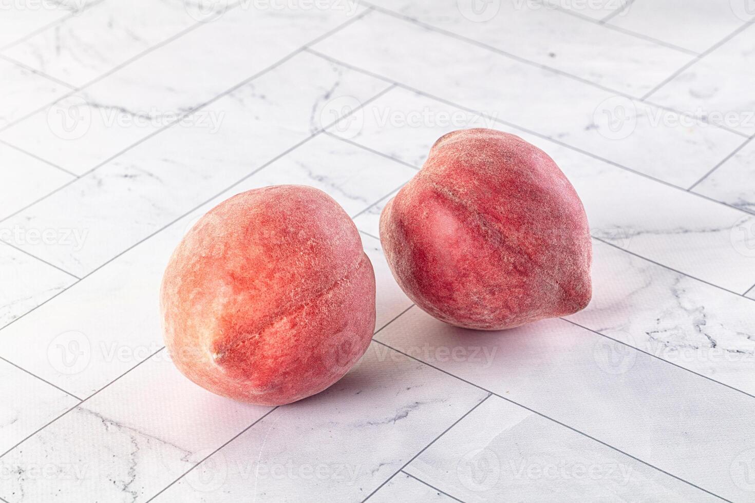 Two peaches sitting on a white marble surface photo