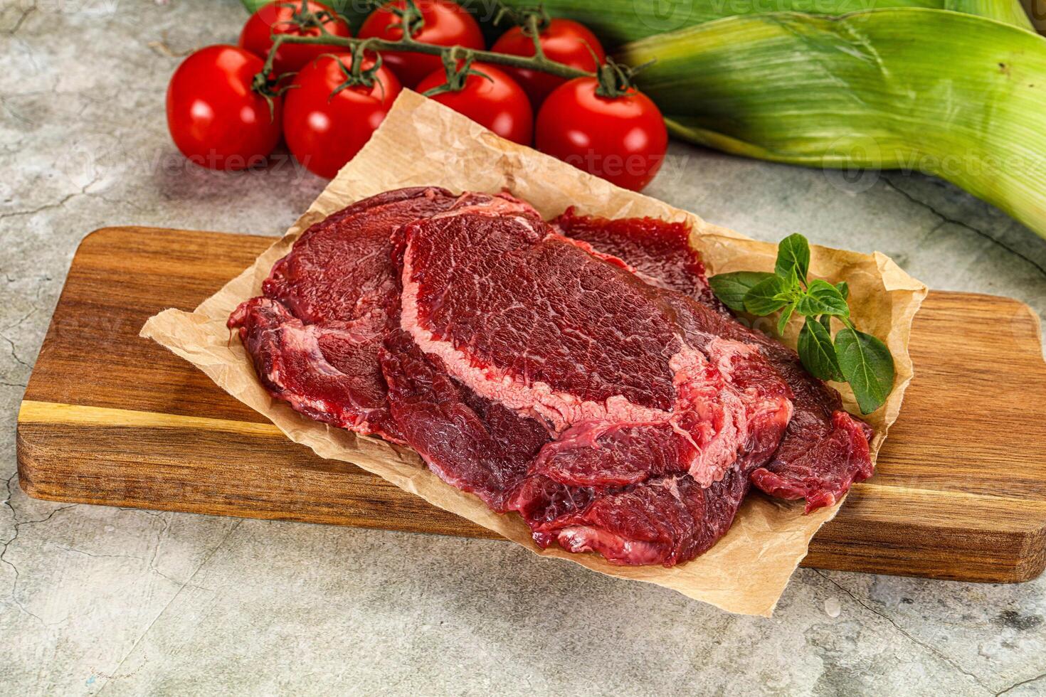 Raw beef on a cutting board with tomatoes and corn photo
