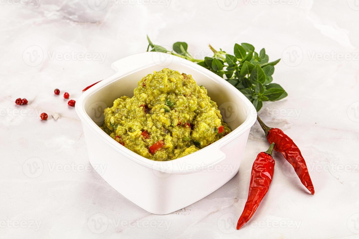 A bowl of green guacamole with red peppers photo