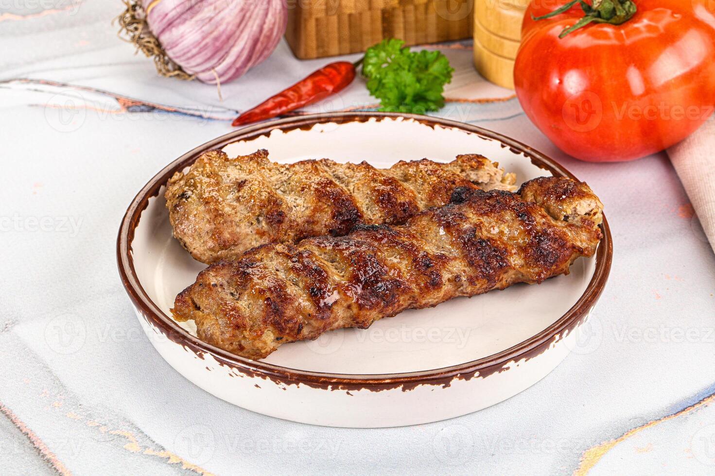 Two grilled meat skewers on a plate with tomatoes and herbs photo