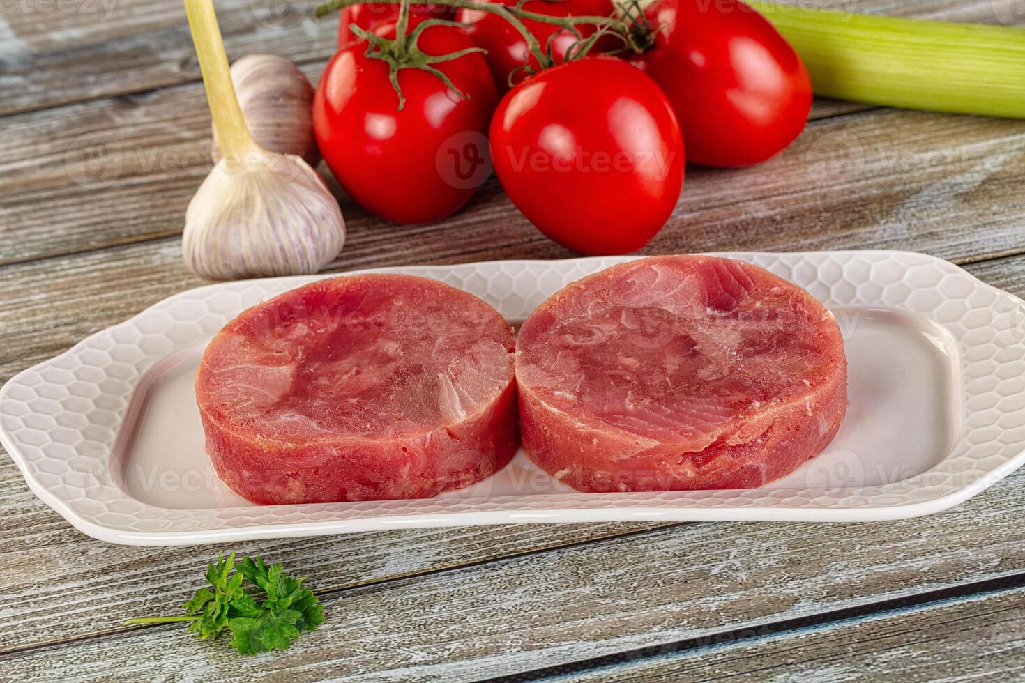 Two raw meat patties on a white plate with tomatoes and garlic photo