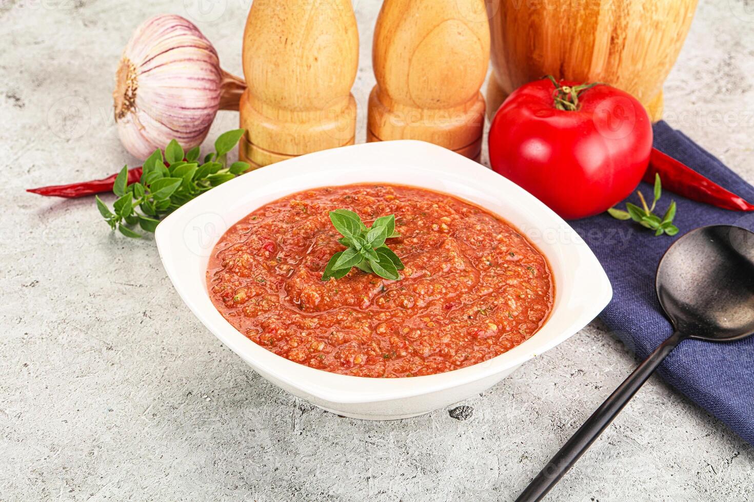 A bowl of tomato sauce next to a spoon and a knife photo