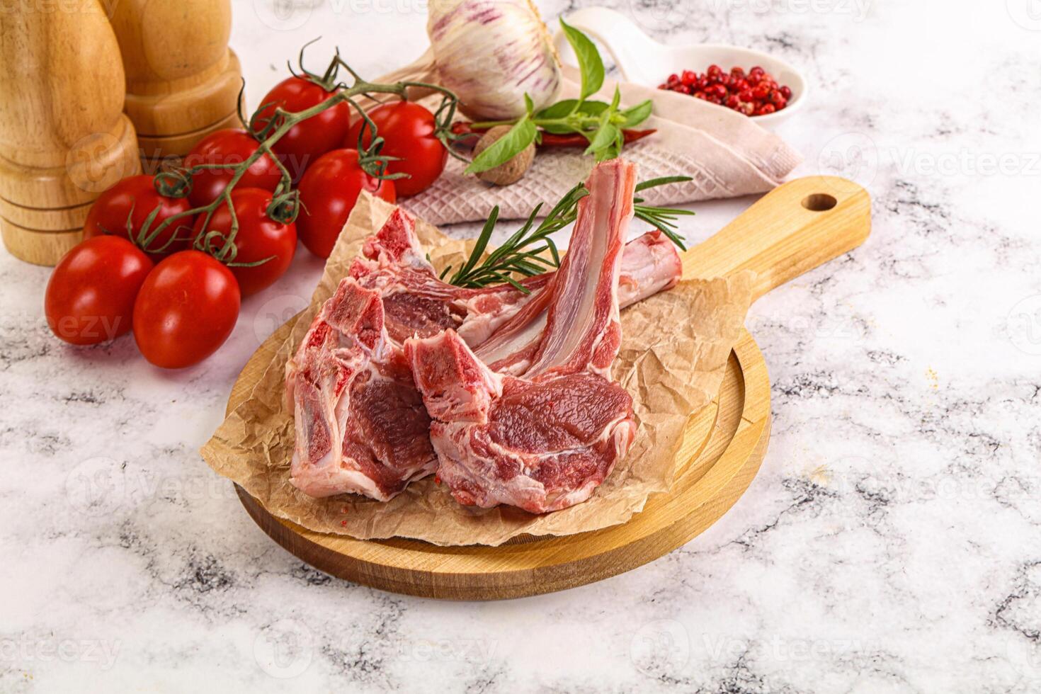 Raw lamb chops on a wooden cutting board with tomatoes and herbs photo