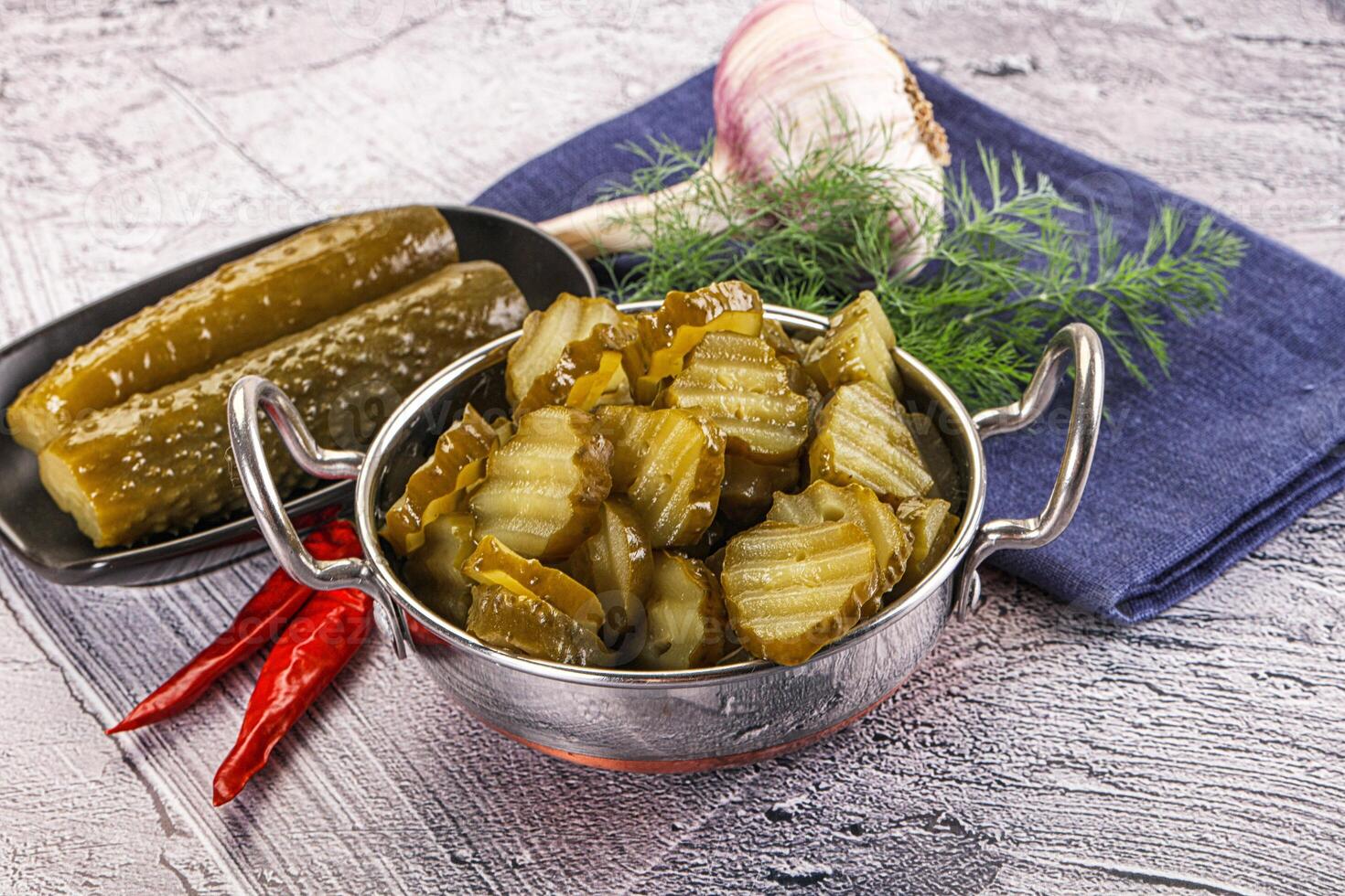 A silver bowl filled with pickles and a knife photo