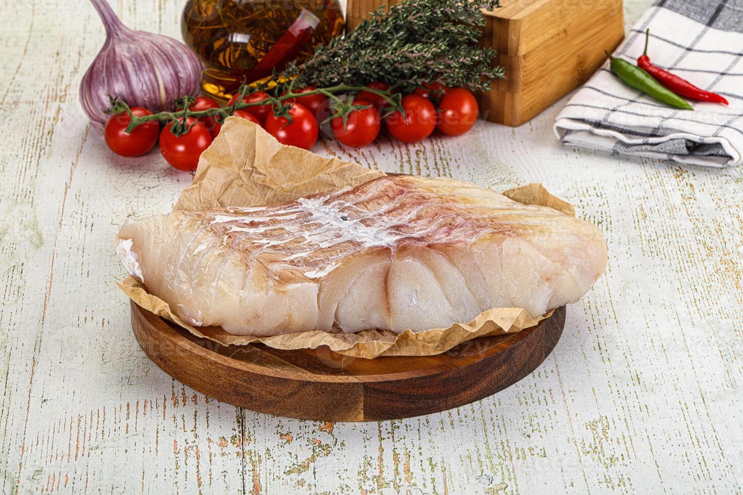 A piece of fish on a wooden cutting board with vegetables and spices photo