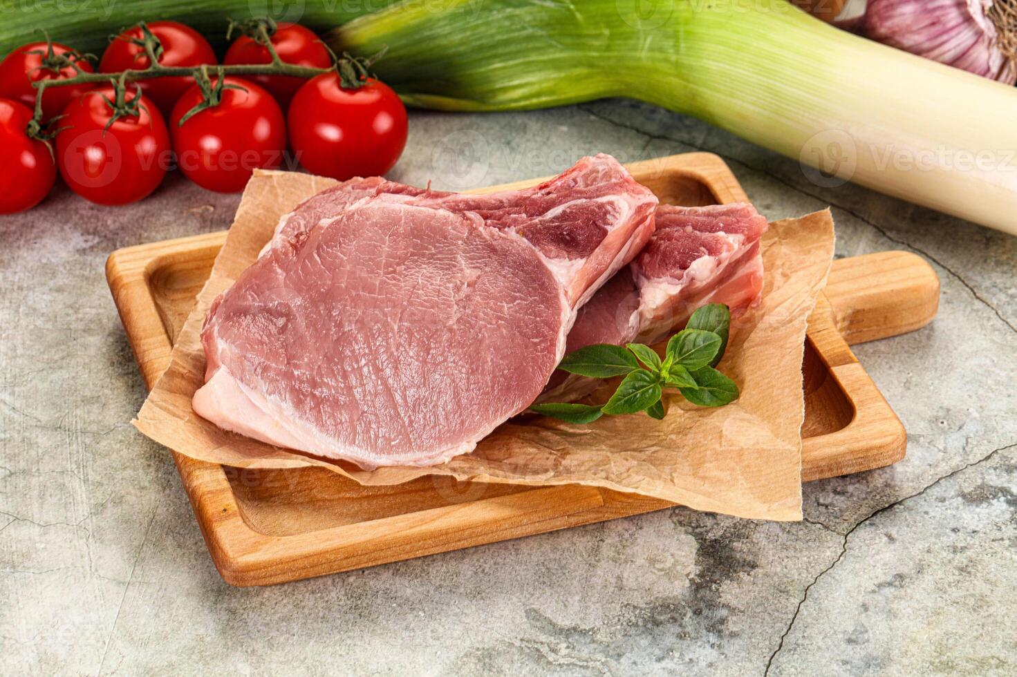 Raw pork chops on a cutting board with tomatoes and vegetables photo