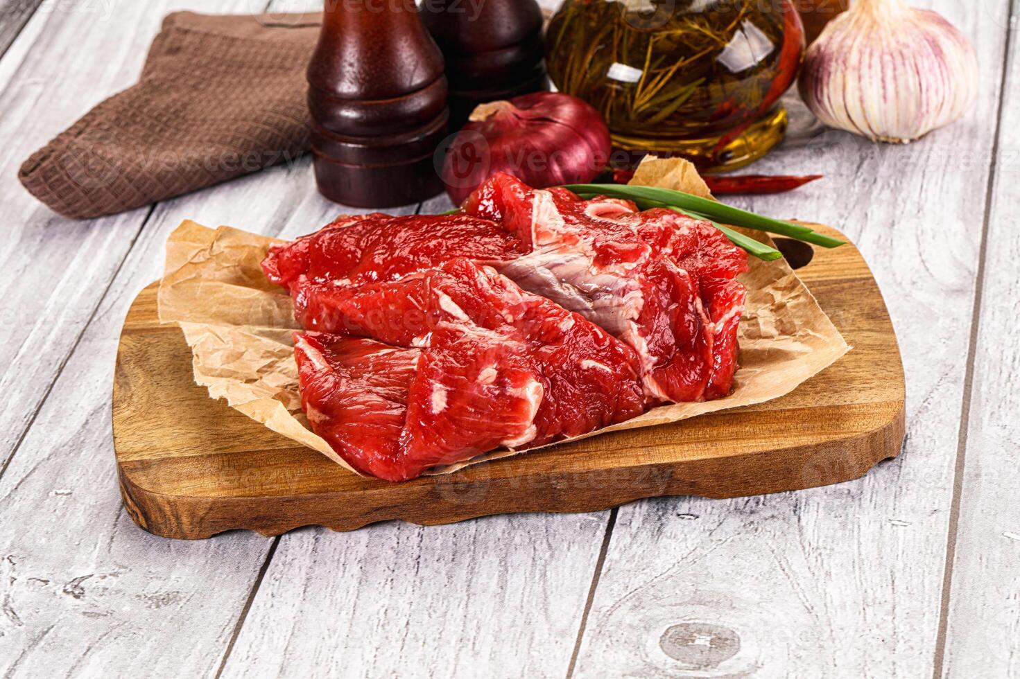 A piece of meat on a cutting board with a bottle of wine and a bottle of pepper photo