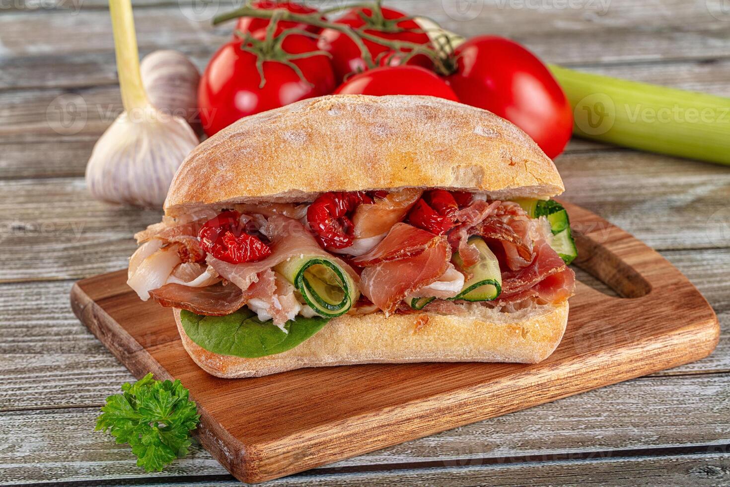 A sandwich with meat, tomatoes and other vegetables on a wooden cutting board photo