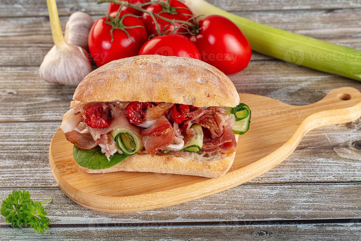 A sandwich on a wooden cutting board with tomatoes and other vegetables photo