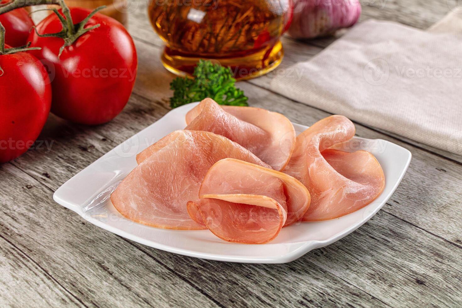 A plate of sliced ham on a table with tomatoes and other ingredients photo