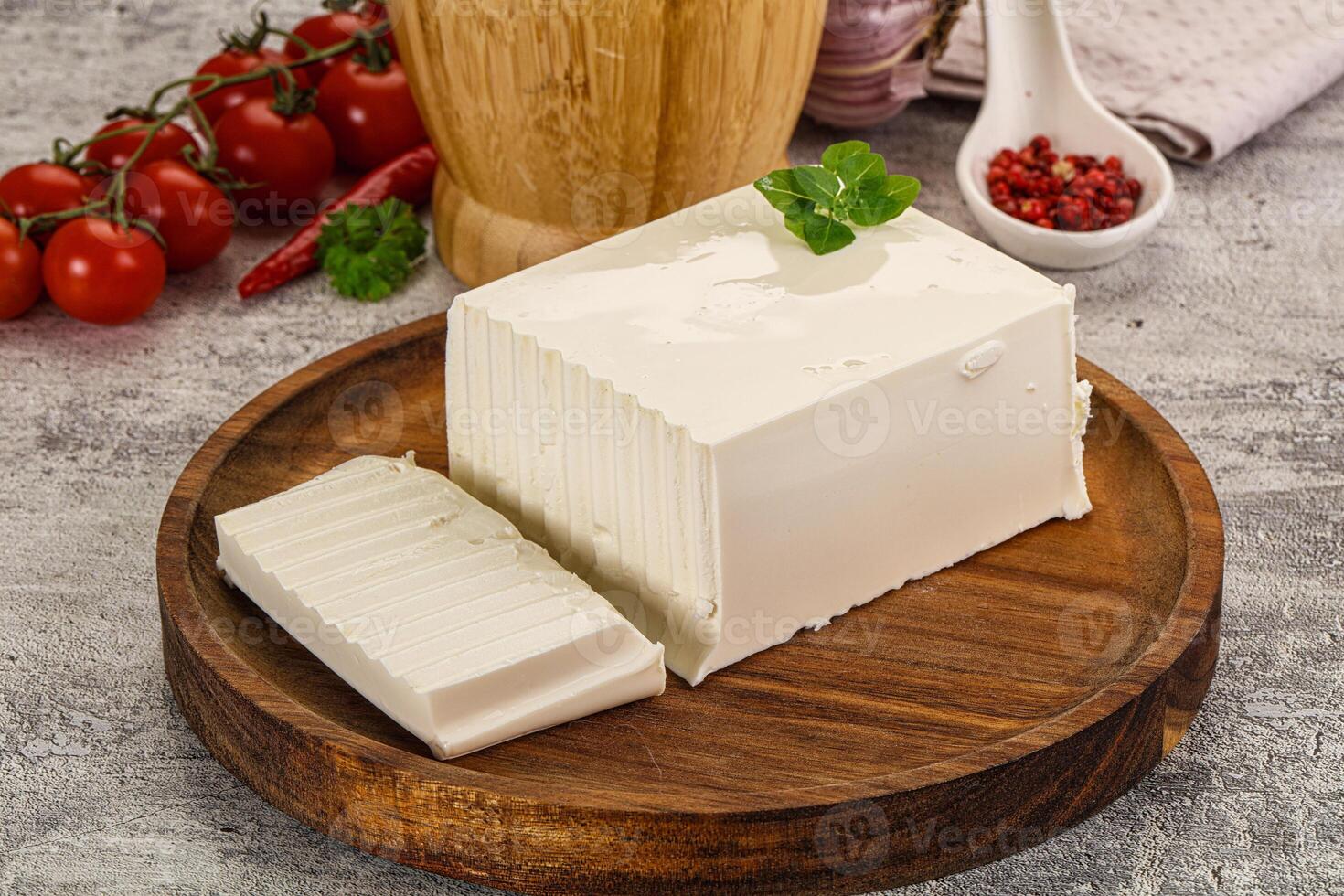 A piece of cheese on a wooden plate with tomatoes and spices photo