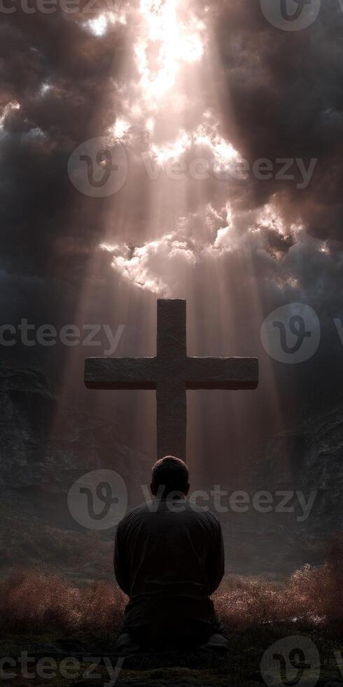 Man kneels in prayer beneath a cross with beams of light photo