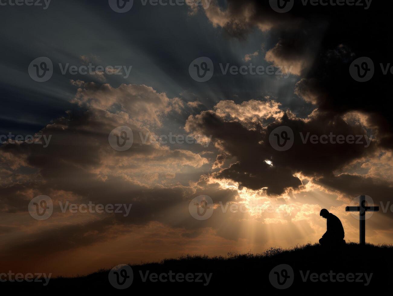 Silhouette of a person kneeling before a cross at sunset photo