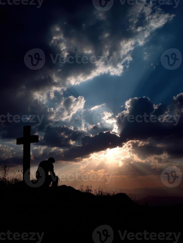 Silhouette of a person praying near a cross at sunset photo