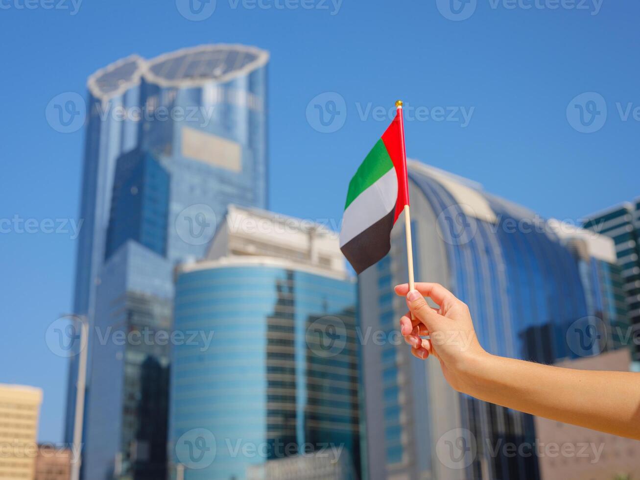hand holding tiny flag of UAE agains city view photo