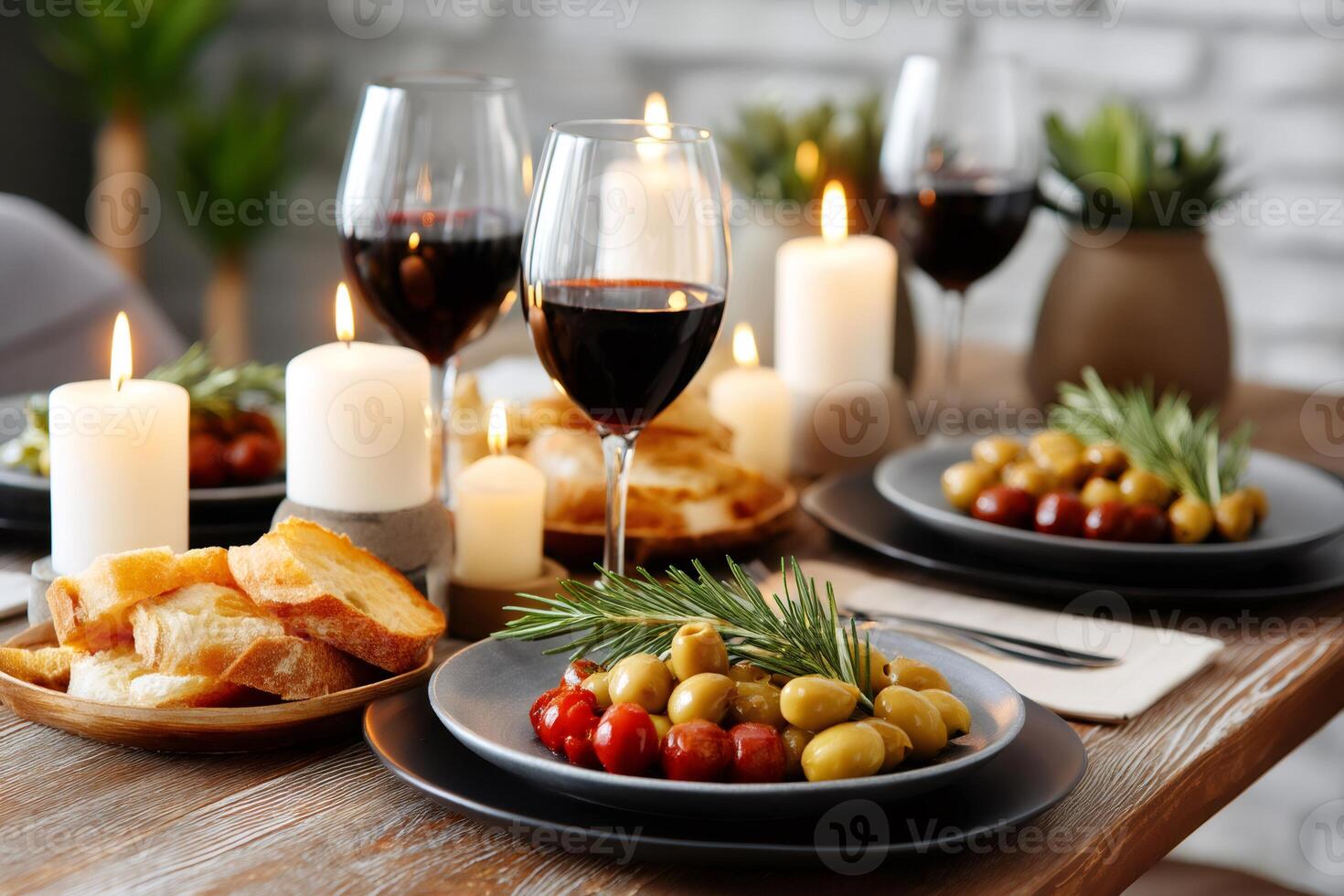 Romantic dinner table setting with red wine, olives, rosemary, candles and bread photo