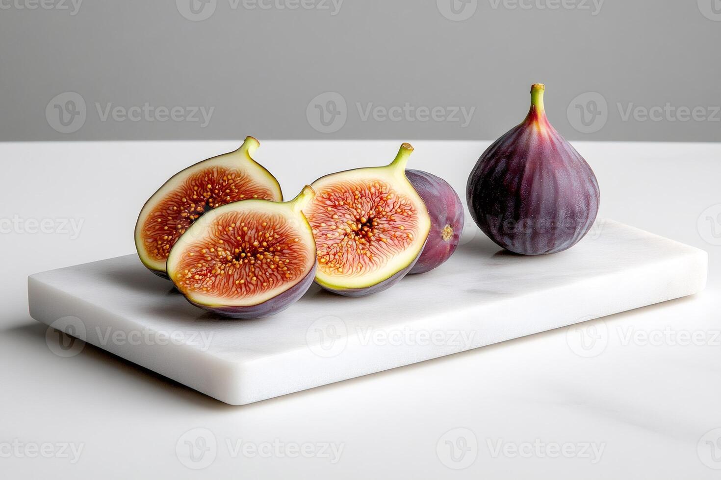Fresh figs exposing their red pulp lie on a white marble cutting board photo