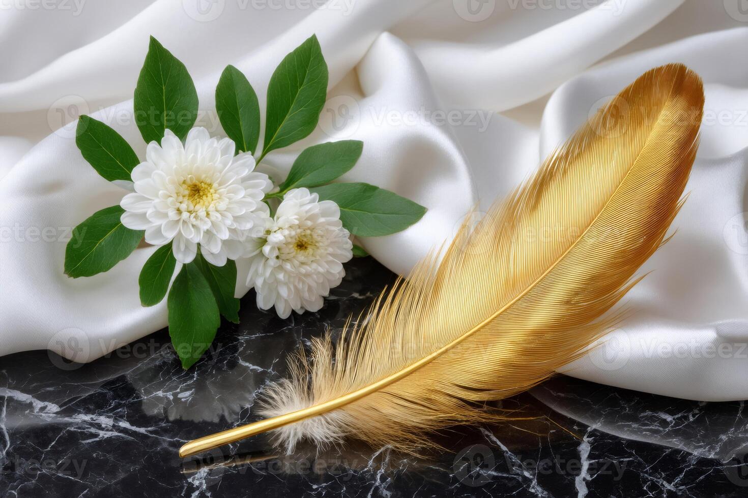 Golden feather and white chrysanthemum flowers resting on black marble and white silk photo