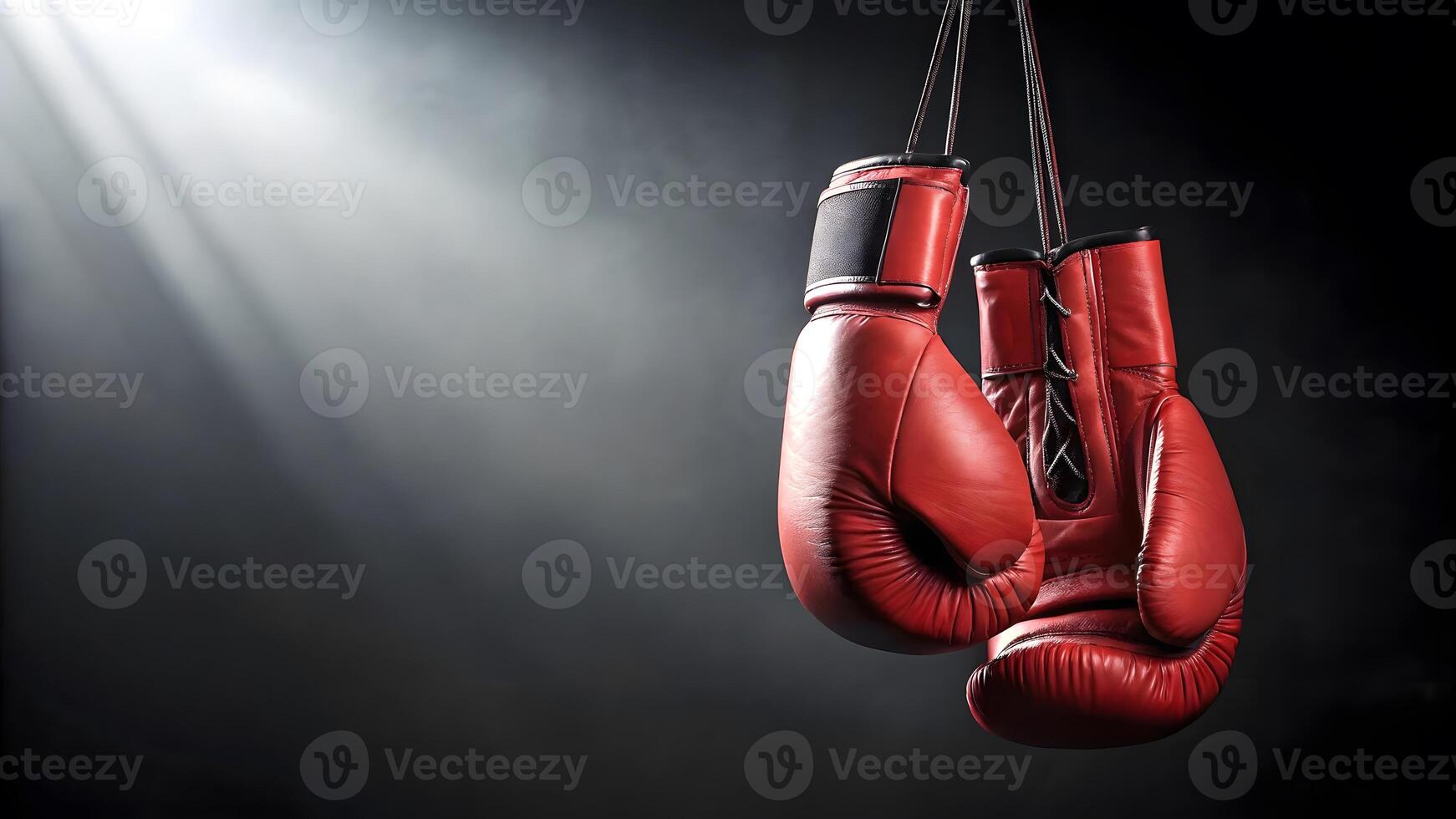 Red boxing gloves hang in dramatic light highlighting their texture and shape photo