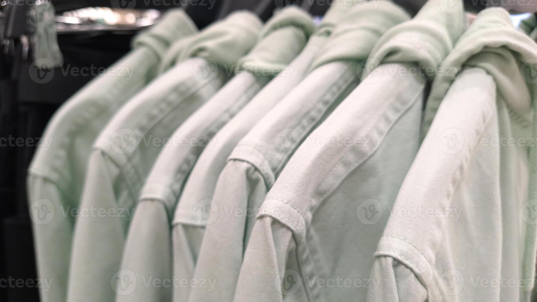 Row of mint green button-up shirts on hangers in clothing store display photo