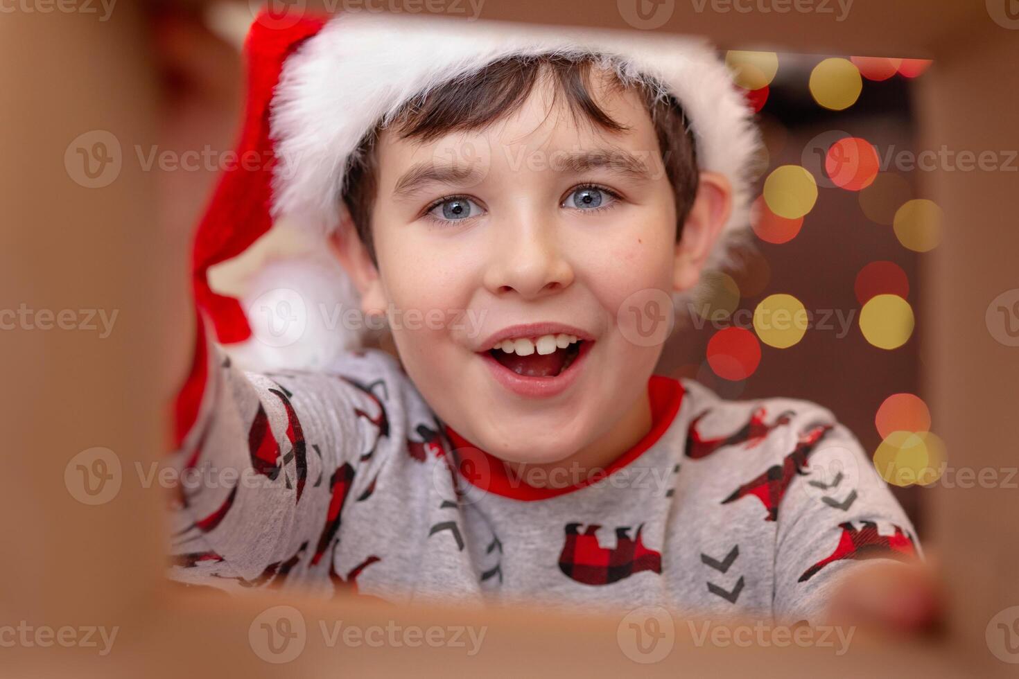A surprised handsome boy in a Santa Claus hat takes a present out of the box photo