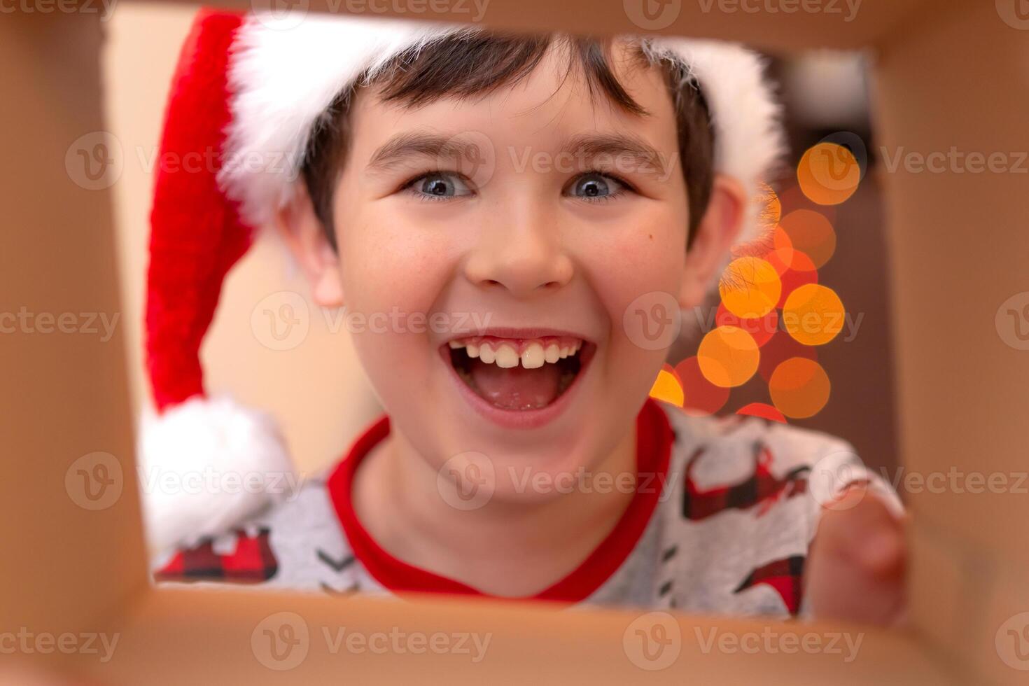 A happy, boy in a New Year's jumper and a Santa Claus hat smashes into a box photo