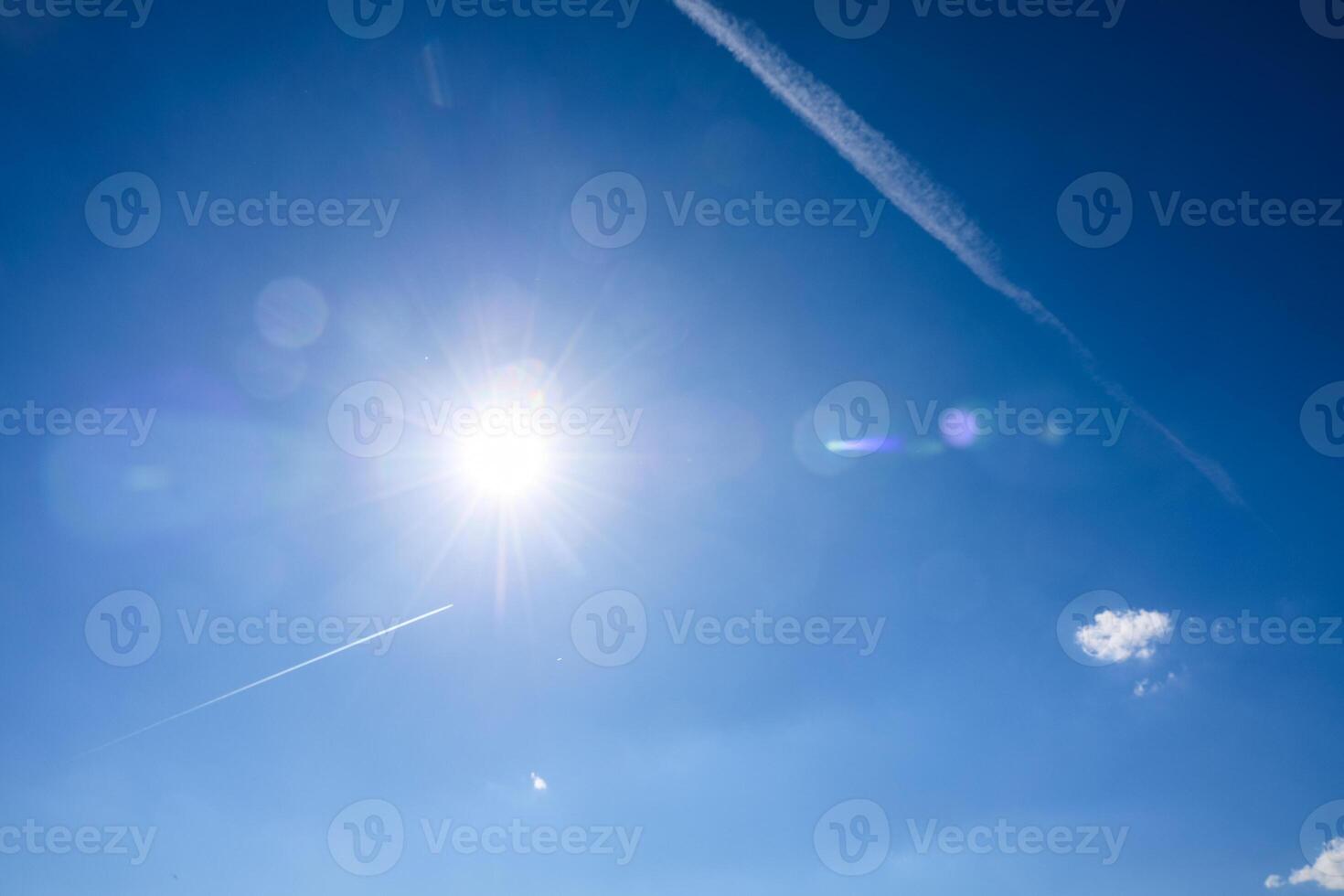 Bright sun shining in a deep blue sky with contrails photo
