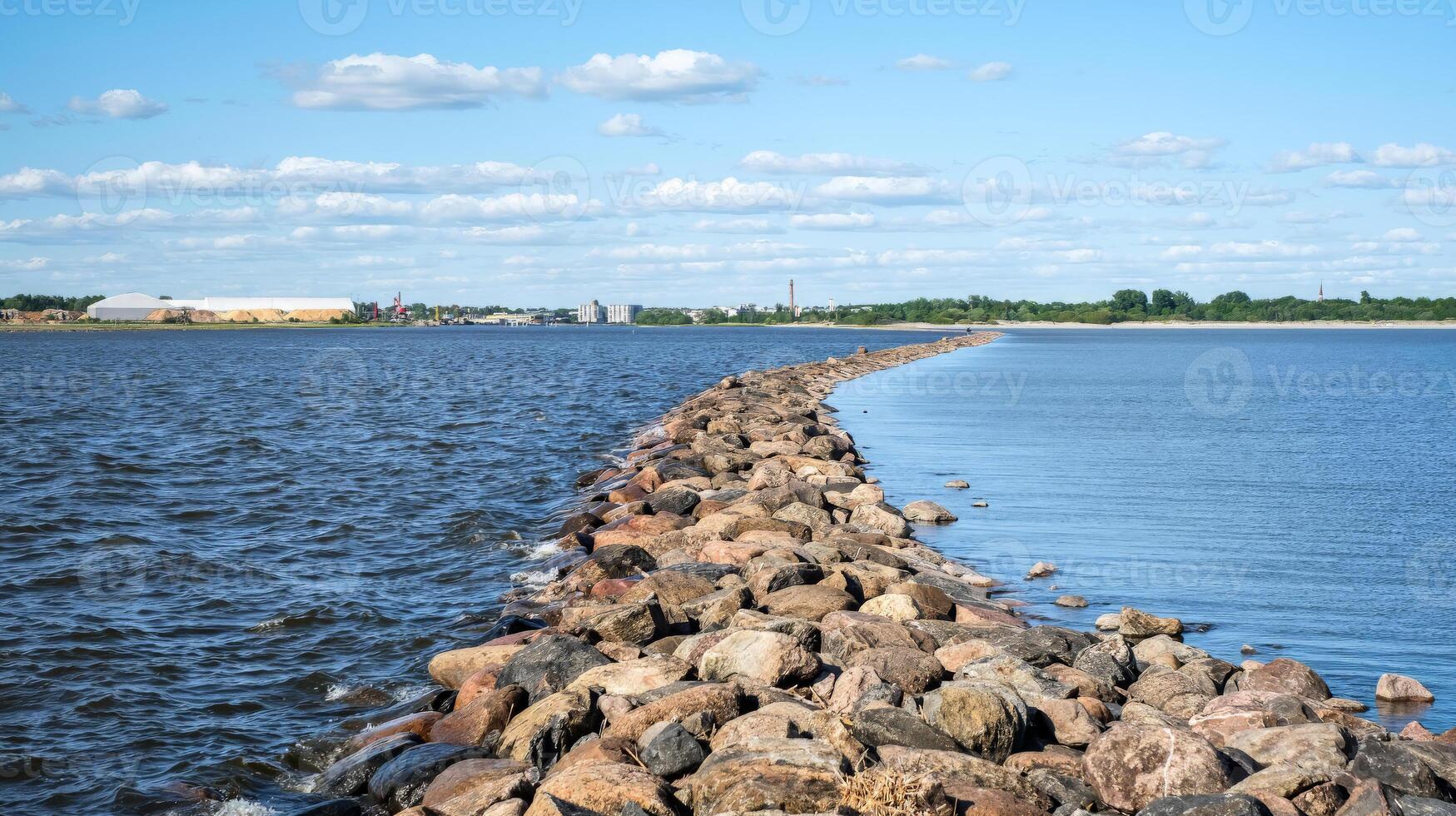 Stone pier stretching across a calm body of water under a bright blue sky with scattered clouds photo