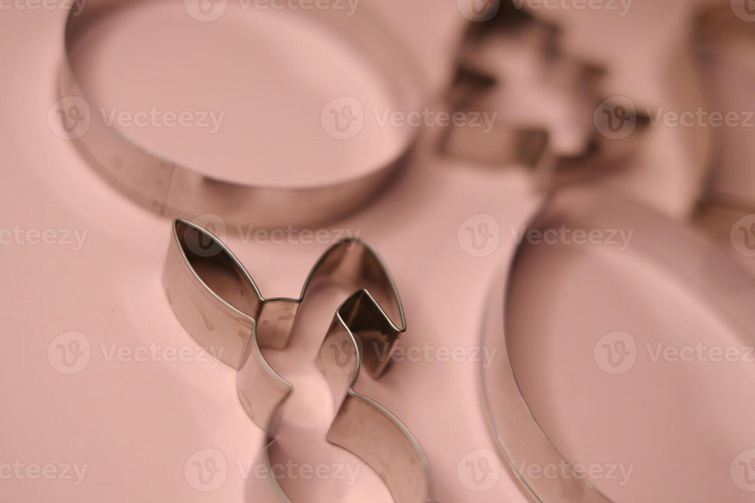 Close-up view of stainless steel cookie cutters in festive shapes, including a bunny and a Christmas tree, placed on a soft pink background photo
