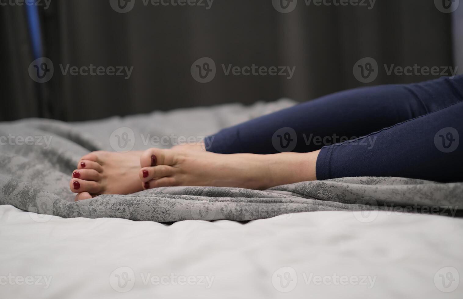 Close-up of a woman's feet with red nail polish, resting on a bed with gray bedding photo