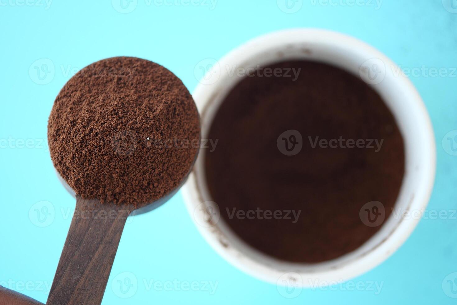 Ground coffee in measuring spoon over container on blue surface photo