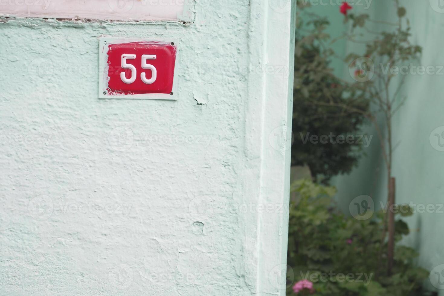 House number 55 displayed on a painted wall in a garden area photo