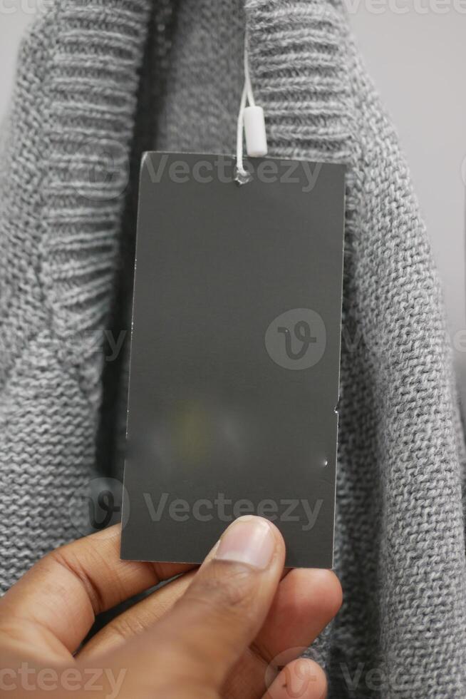 Gray sweater with an attached price tag being held up by a hand photo